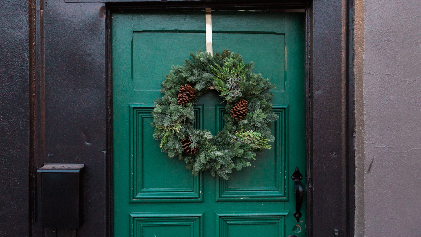 Festive holiday wreath with pinecones and evergreens hanging on a classic green Toronto doorway.