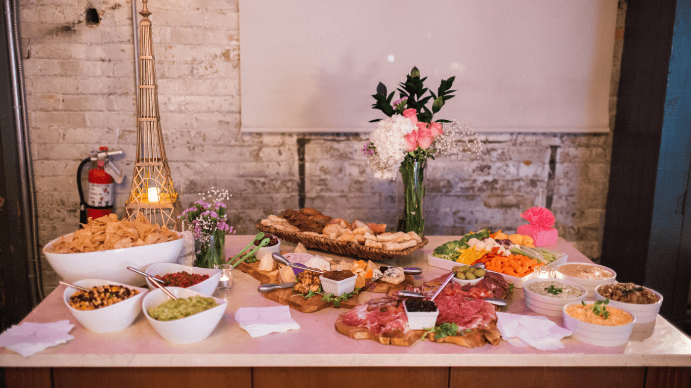  Elegant catering spread with charcuterie boards, fresh vegetables, dips, and breads, styled with flowers for a professional event.
